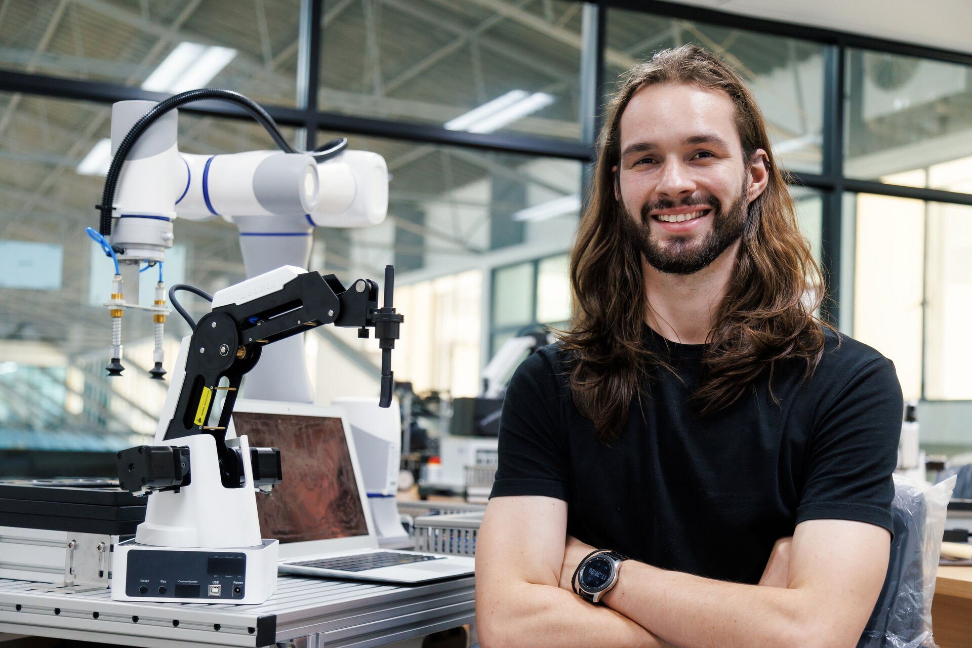 Junger Mann mit langen braunen Haaren, der neben einem Roboter steht