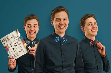 Junger, lachender Mann mit dunklem Hemd und blauer Fliege, einmal im Vordergrund, zweimal im Hintergrund. Mann im Hintergrund links hält Filmklappe