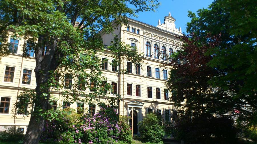vordere Gebäudeansicht mit Bäumen und Sträuchern